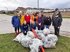 The image shows a group of people, dressed in warm clothing, standing together on a grassy roadside, surrounded by various plastic bags and bottles.

AI-generated content may be incorrect.