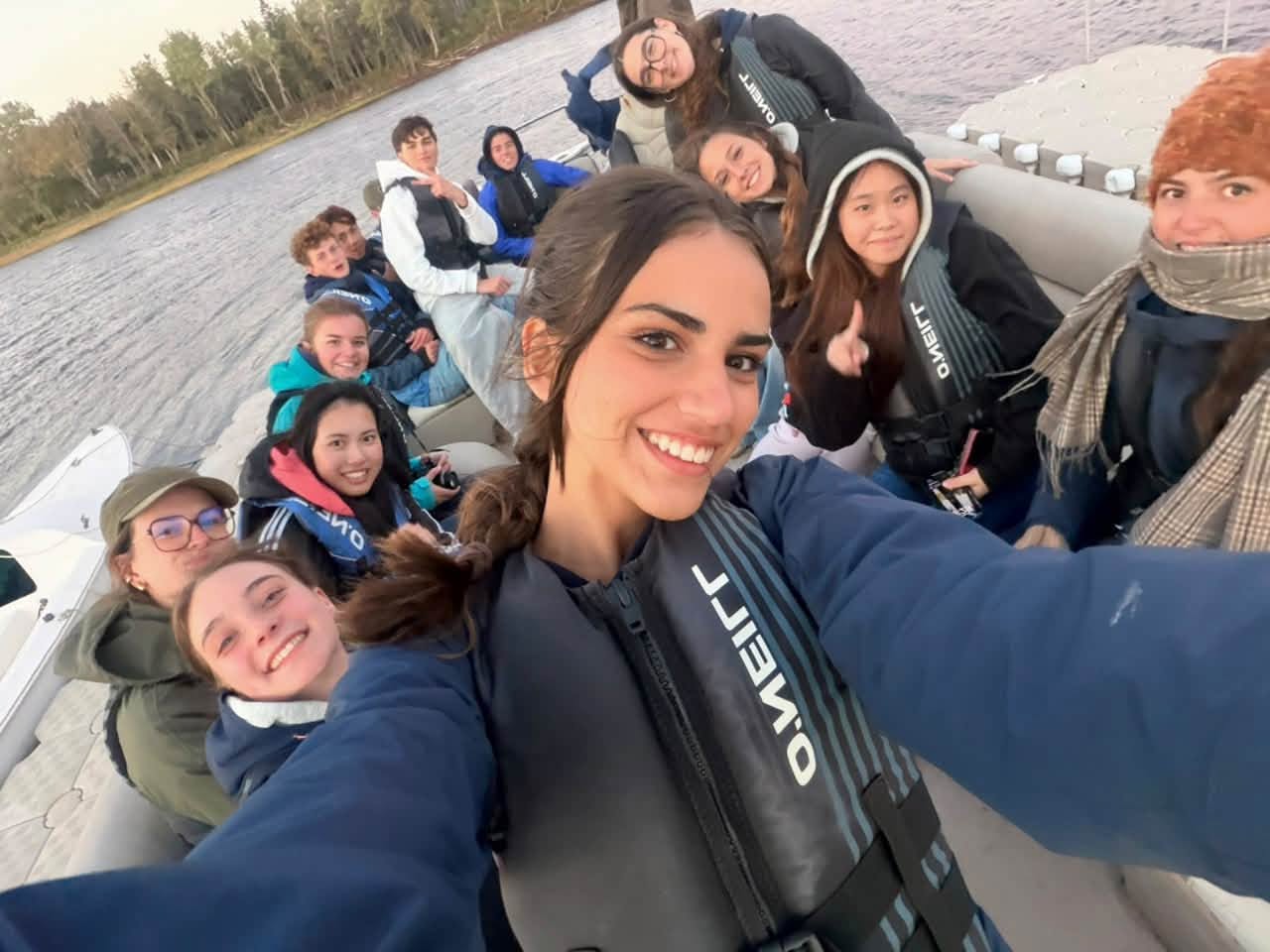 picture of a lady smiling taking a selfie with group of other boys and girls on a boat. They are all smiling.