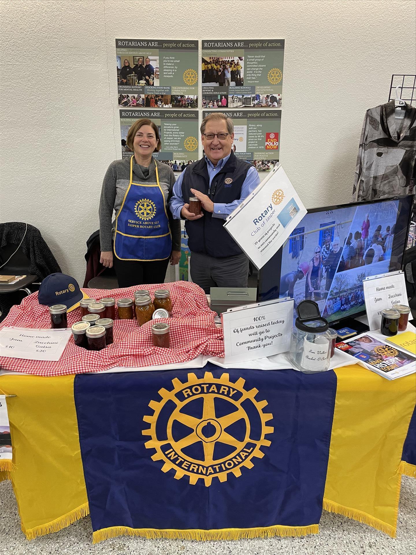Two Rotarians stand in front of a booth adorned with a yellow and blue banner  