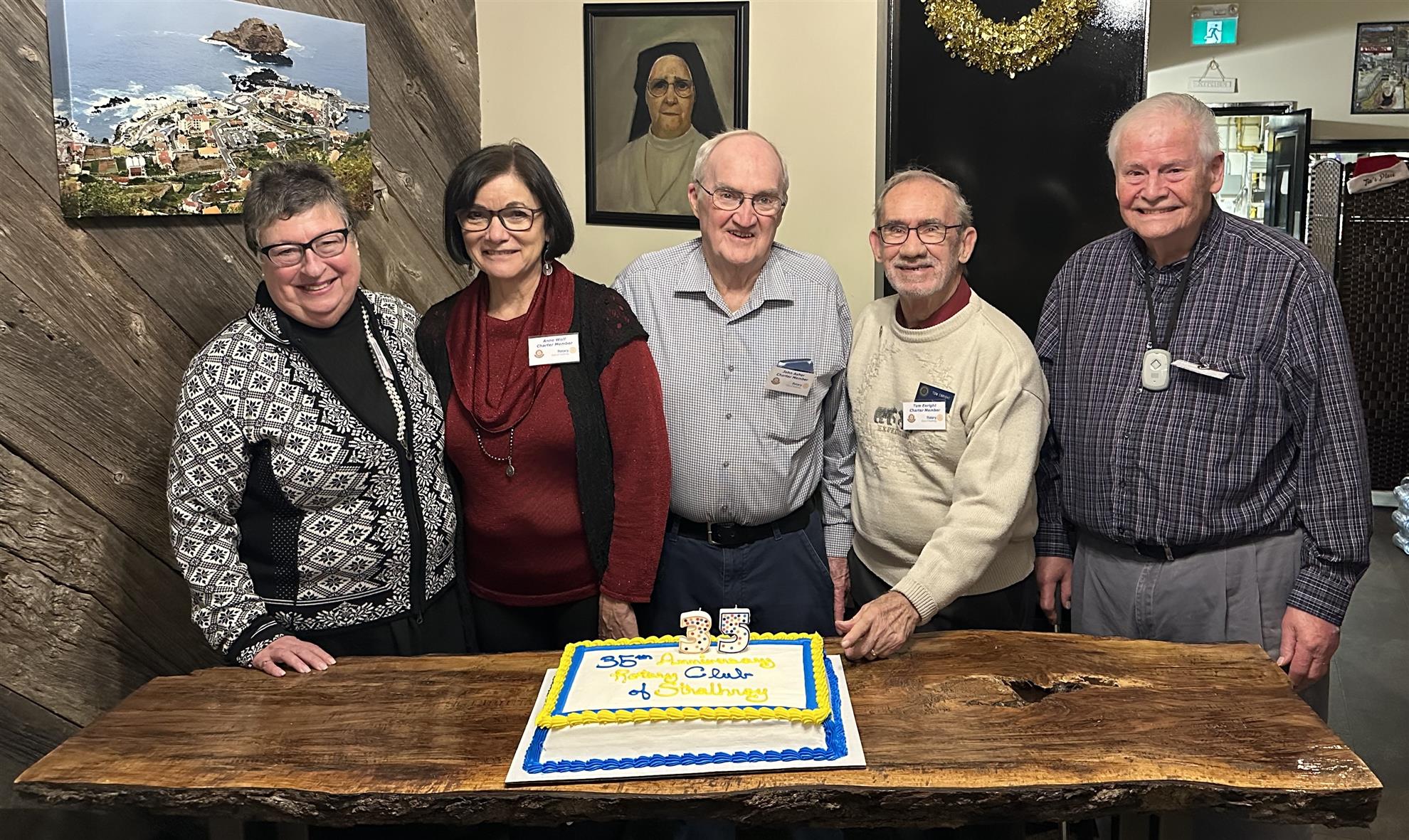 Several original charter members of the Strathroy Rotary Club pose for a photo in front of a cake commemorating the 35th anniversary of our charter.