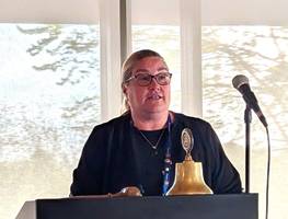 A person standing at a podium with a bell and a bellDescription automatically generated