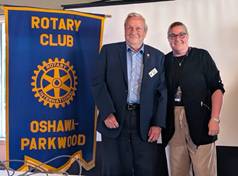 A person and person standing in front of a bannerDescription automatically generated