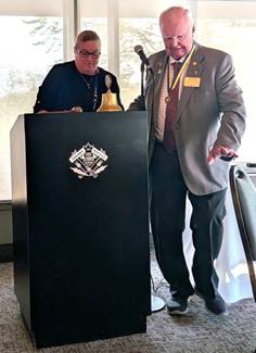 A person standing at a podium with a bell and a person standing at the podiumDescription automatically generated