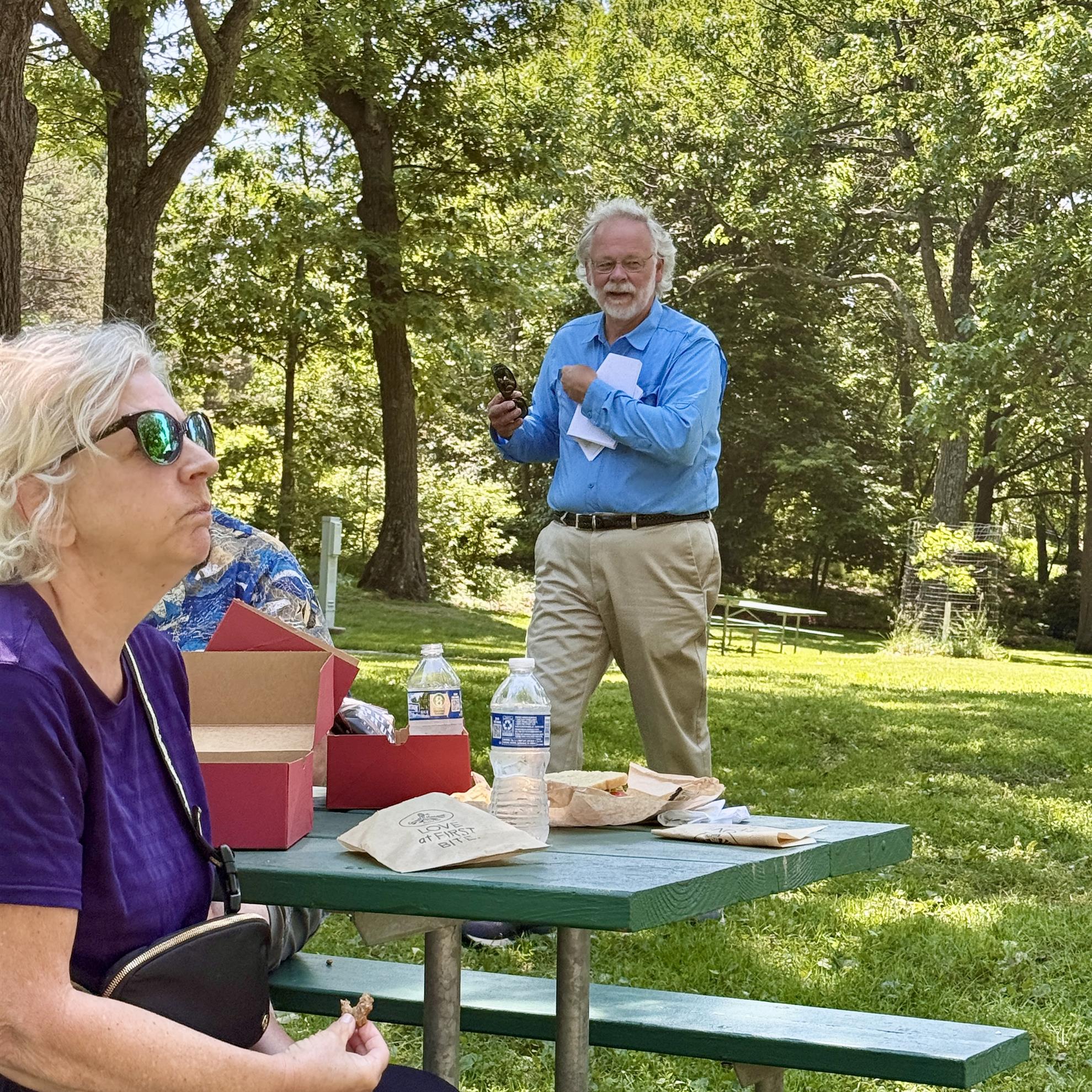 A person standing next to a person at a picnic tableAI-generated content may be incorrect.
