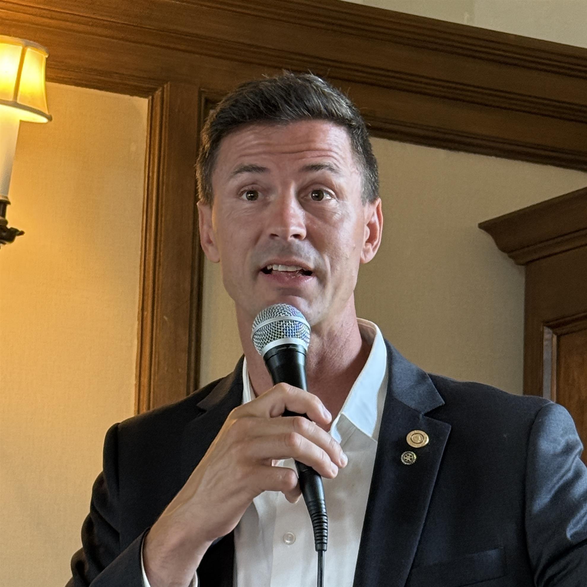 A person in a suit holding a microphoneAI-generated content may be incorrect.