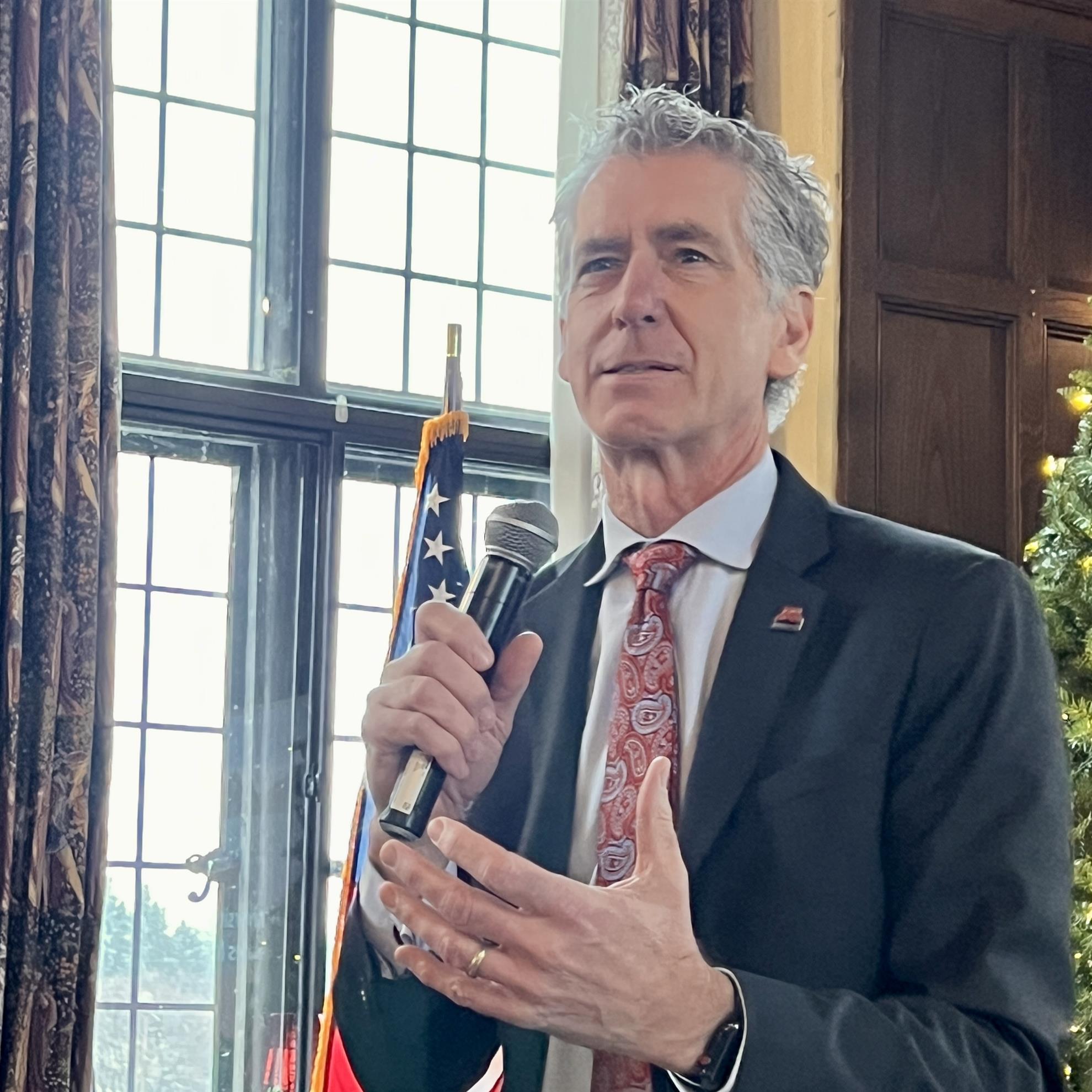 A person in a suit holding a microphoneDescription automatically generated