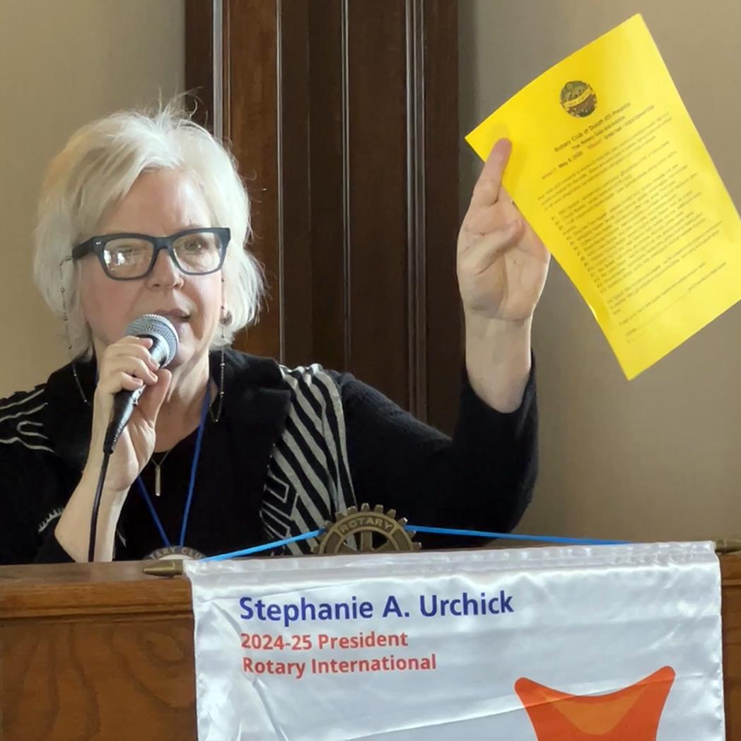 A person holding a microphone and holding a yellow paperAI-generated content may be incorrect.