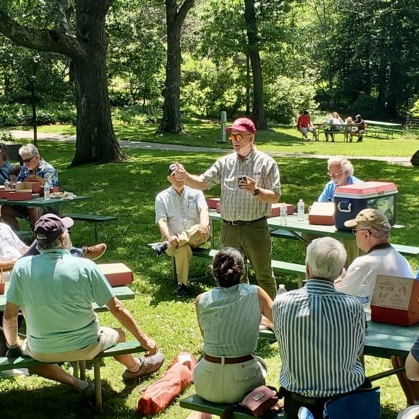 A person standing in front of a group of people sitting at picnic tablesAI-generated content may be incorrect.