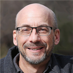 A person wearing glasses and smilingDescription automatically generated