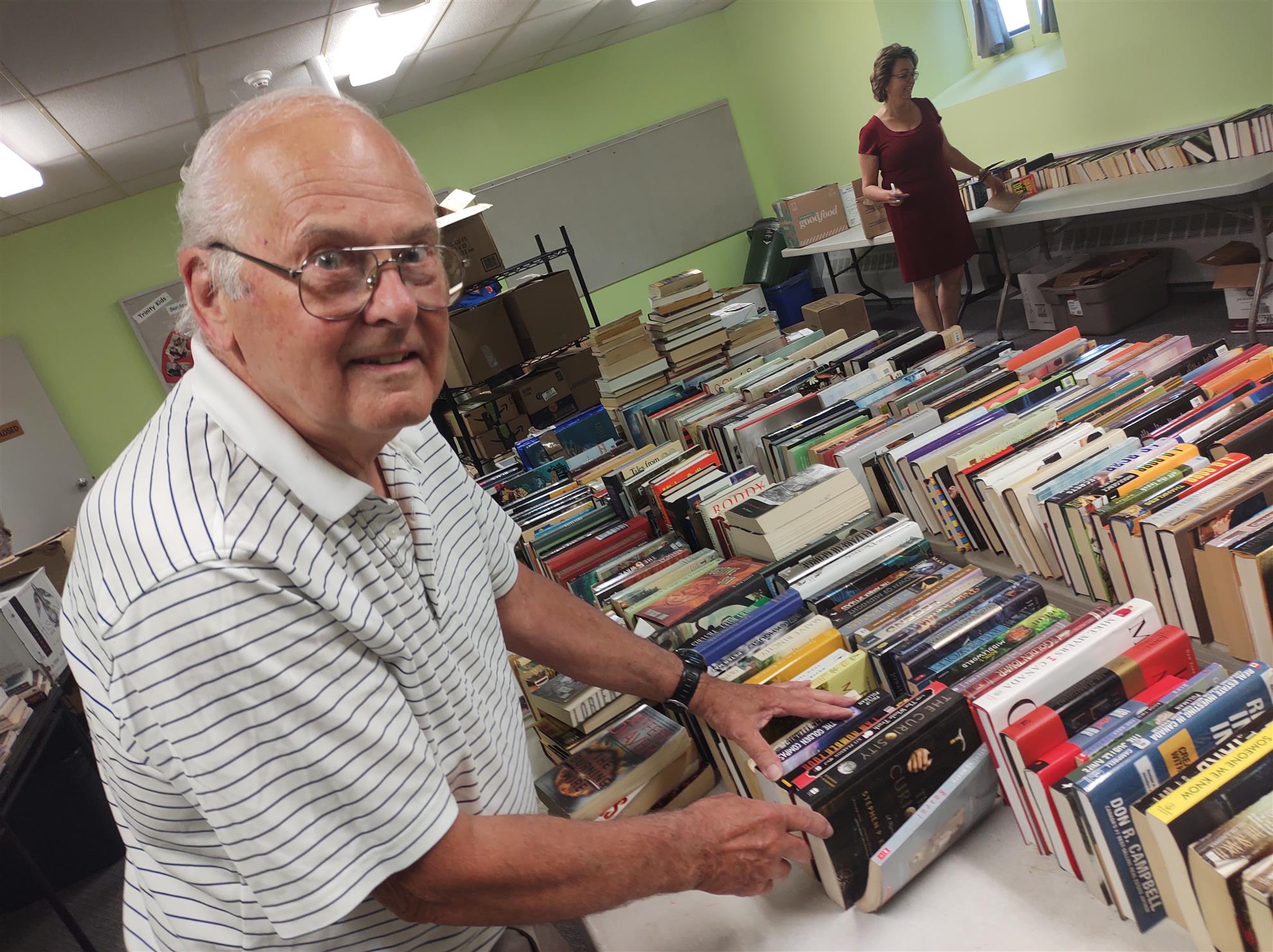A man smiles for the camera while sorting a table filled with books.