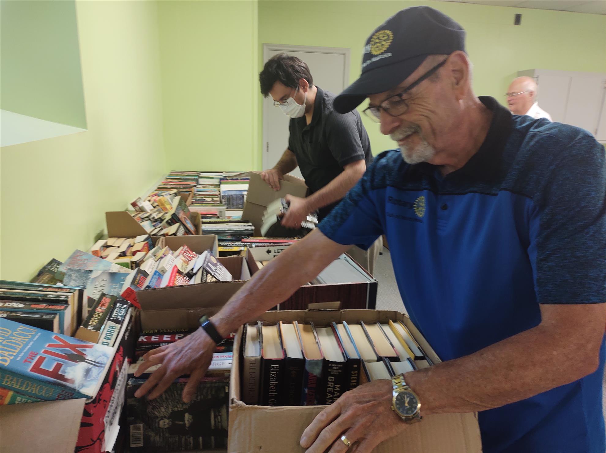 2 Rotarians sort a large table of books.