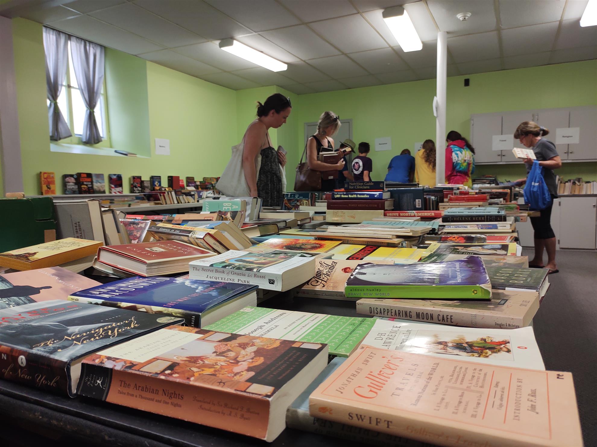 Seven people, including teens and adults, browse through tables filled with used books inside a church basement.