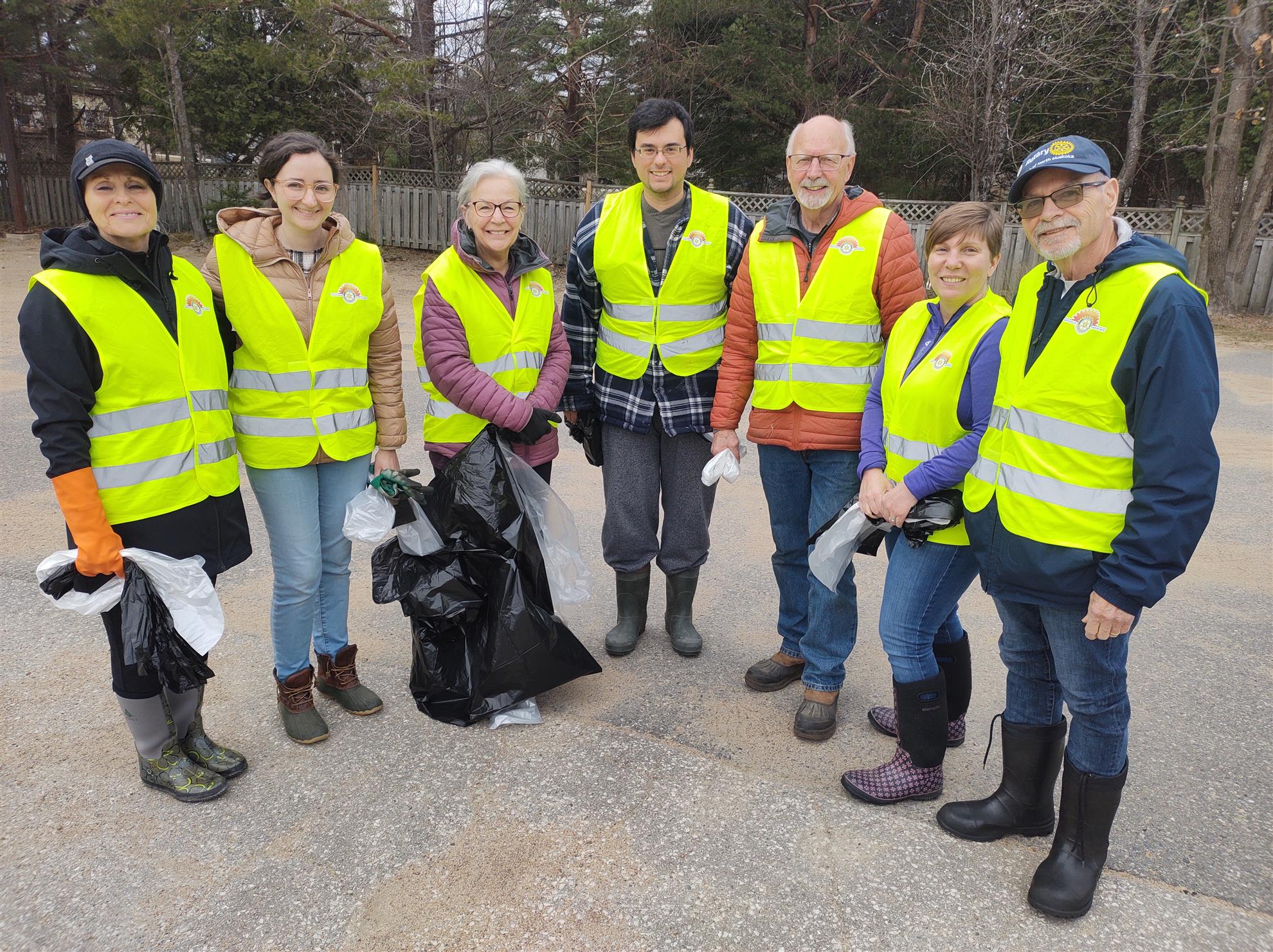 A group of smiling people in yellow reflective vests holding empty black garbage bags.