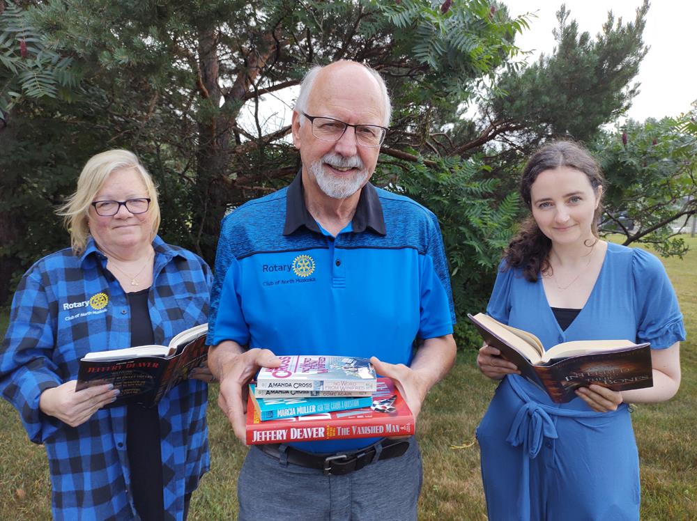 A woman, man, and woman in blue shirts with Rotary logos hold books.