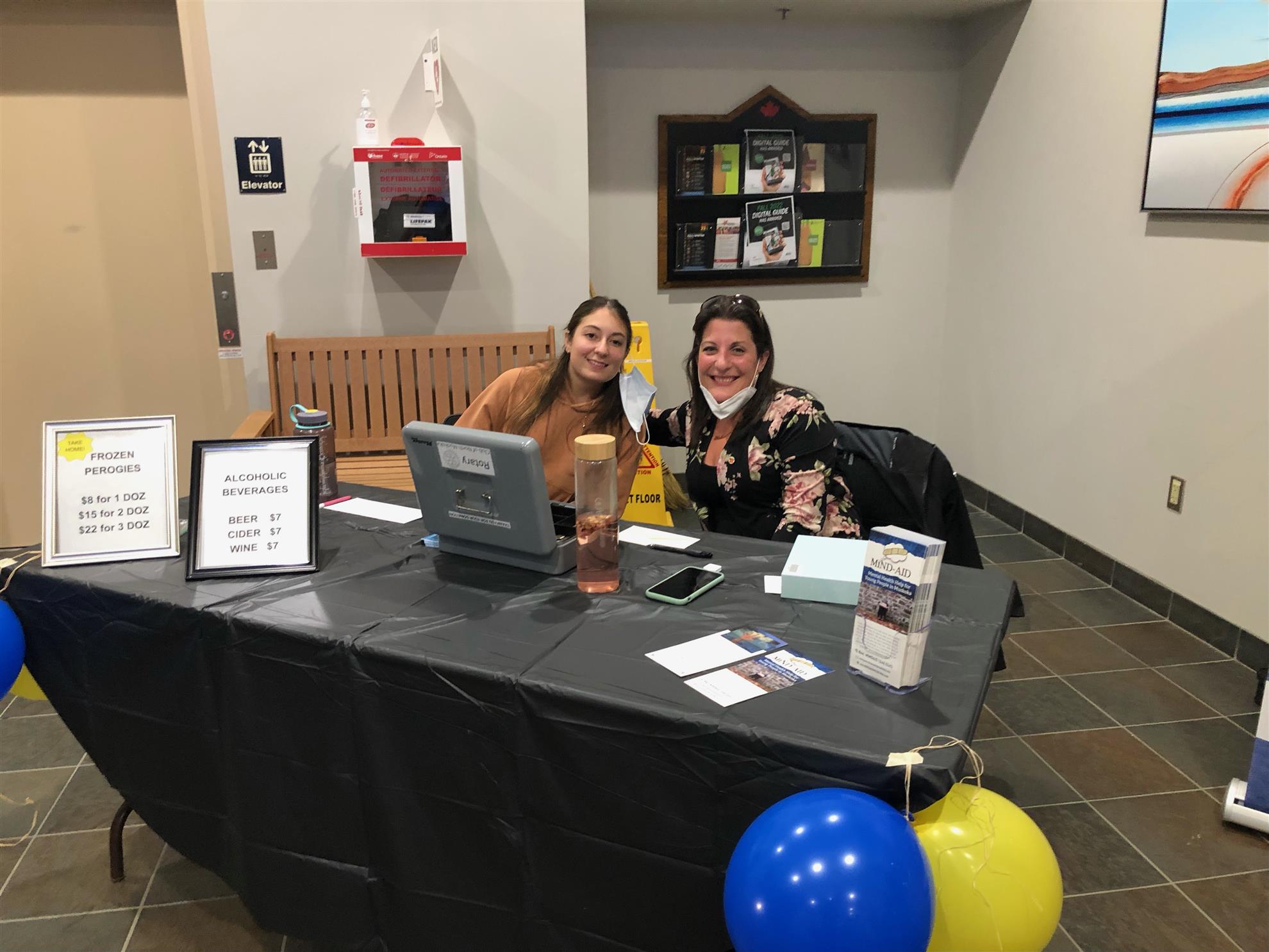 two smiling woman seated at a table. they are selling event tickets.