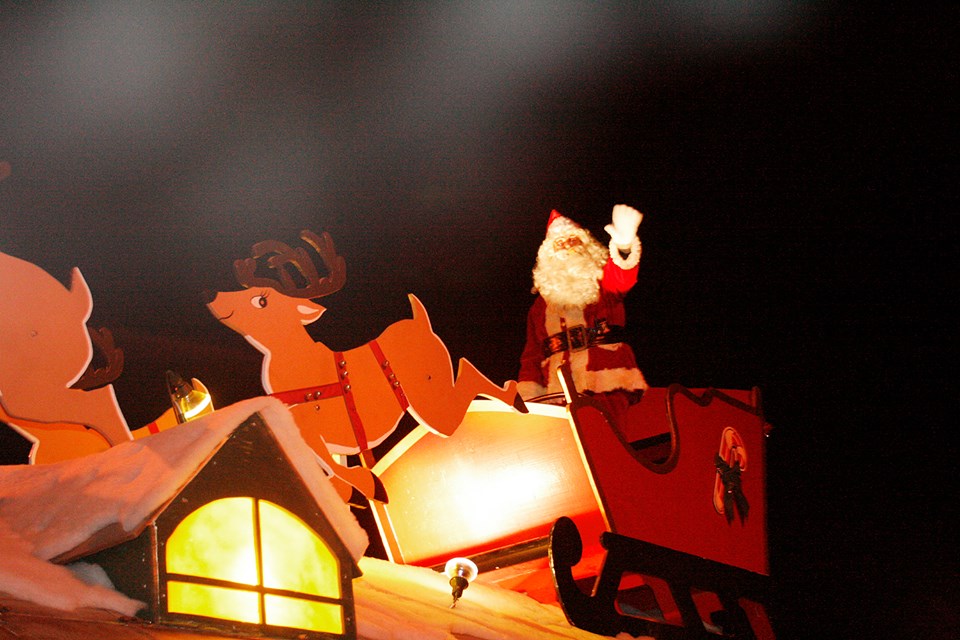 Santa waves from an illuminated parade float during a nighttime parade.