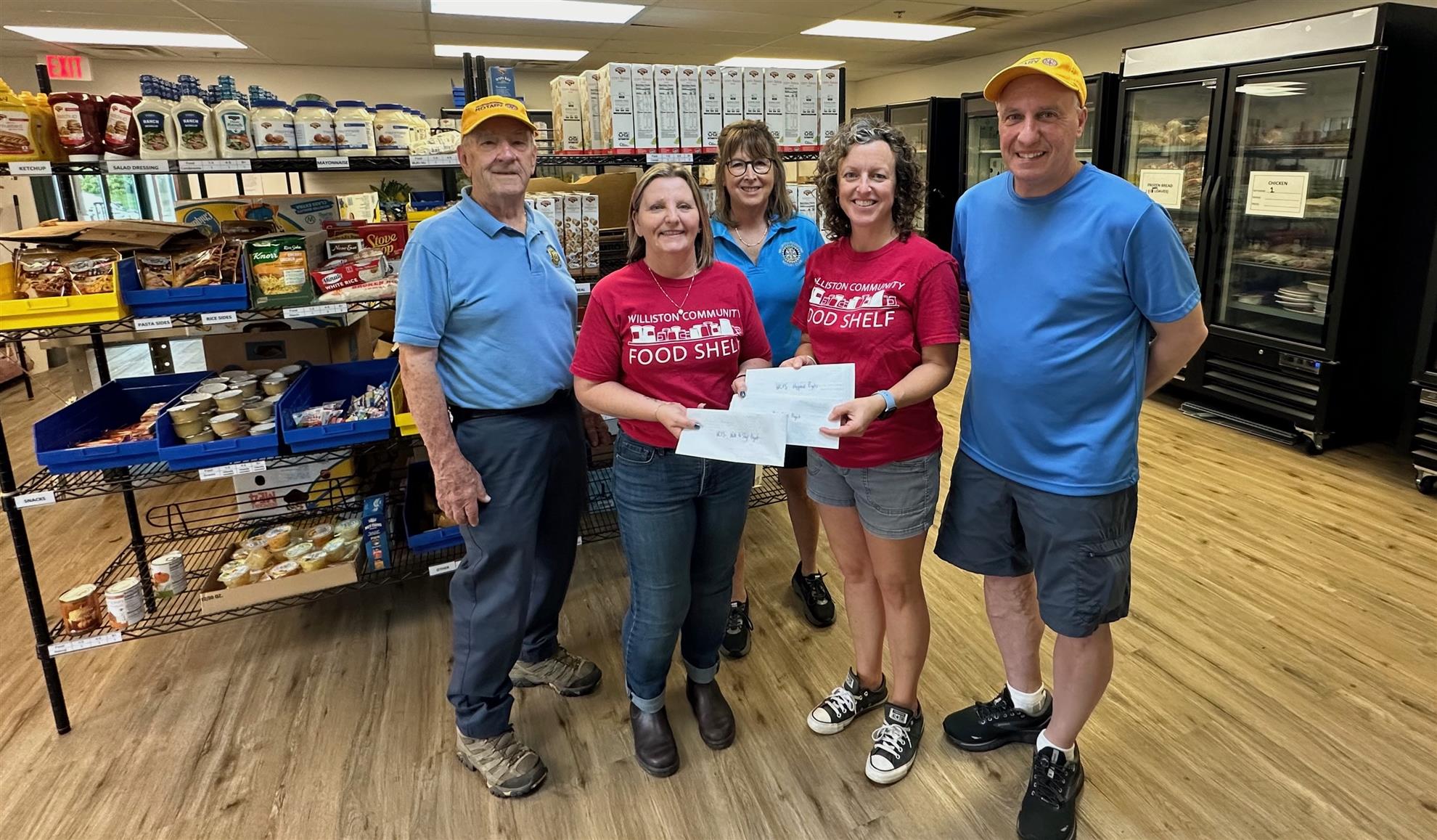 two women in red food shelf t-shirts hold grant checks given by three Rotary members in blue shirts