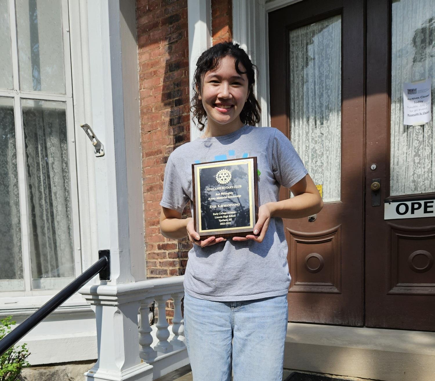 Evie poses with her recipient plaque on the sairs of the Ypsilanti Historical Museum