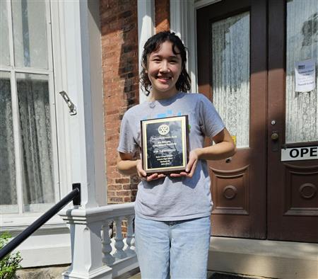 Evie poses with her recipient plaque on the sairs of the Ypsilanti Historical Museum