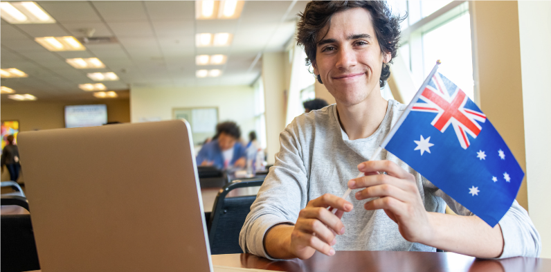 young person at laptop with australian flag in hand