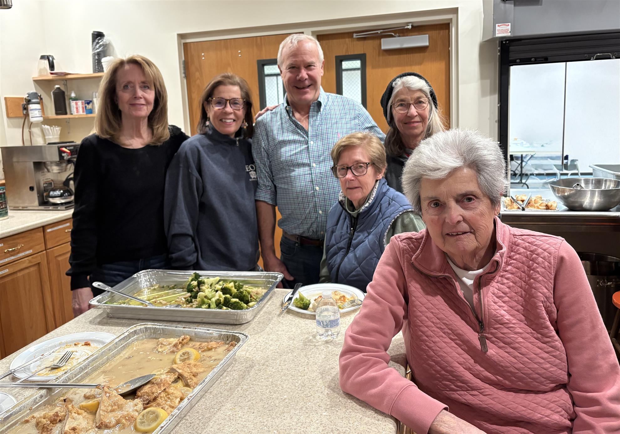 People sitting and standing around a counter filled with food