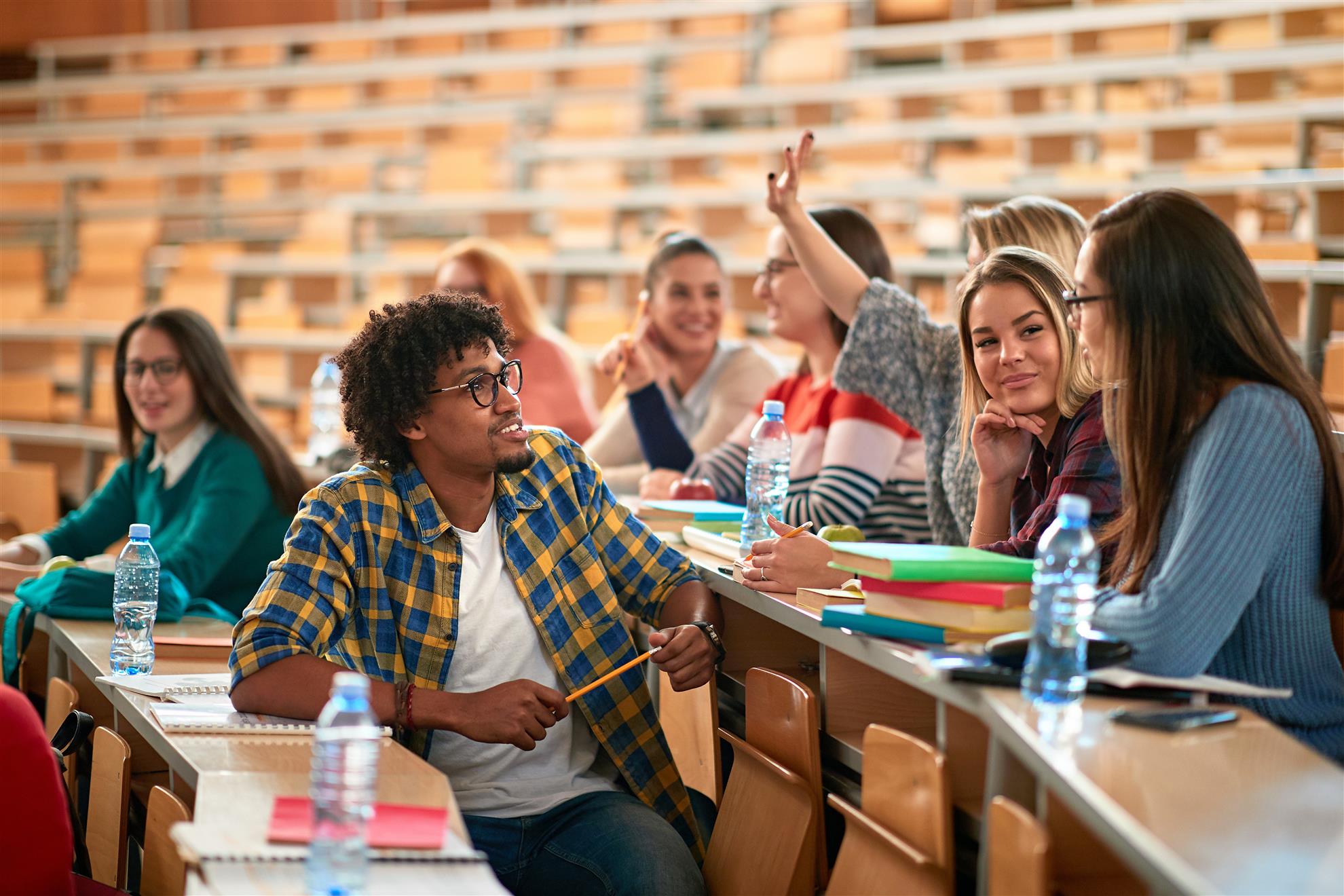 a group of male and female students sit and talk in a large theater style classroom.