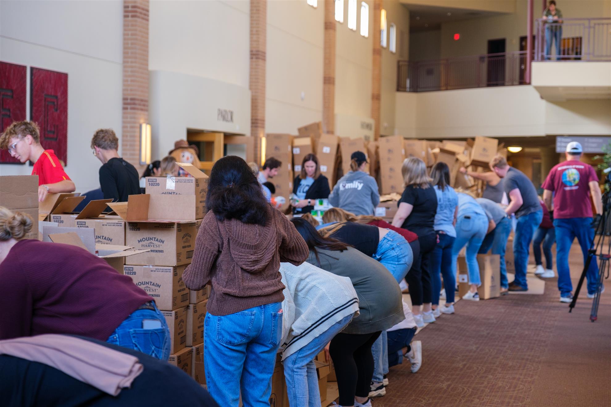 A group of volunteers gather in a church hall to assemble boxes of food.
