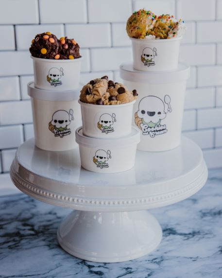 Photo of Cookies and Cream company's ice cream samples In front, a medium-sized bowl has a lid on it, and a smaller bowl is on top of it with a scoop of ice cream on it. Behind the front pile of bowls are two other ice cream towers, with a tall cup of ice cream at the bottom and another small bowl of ice cream without a lid and two scoops of ice cream on top of them.. 