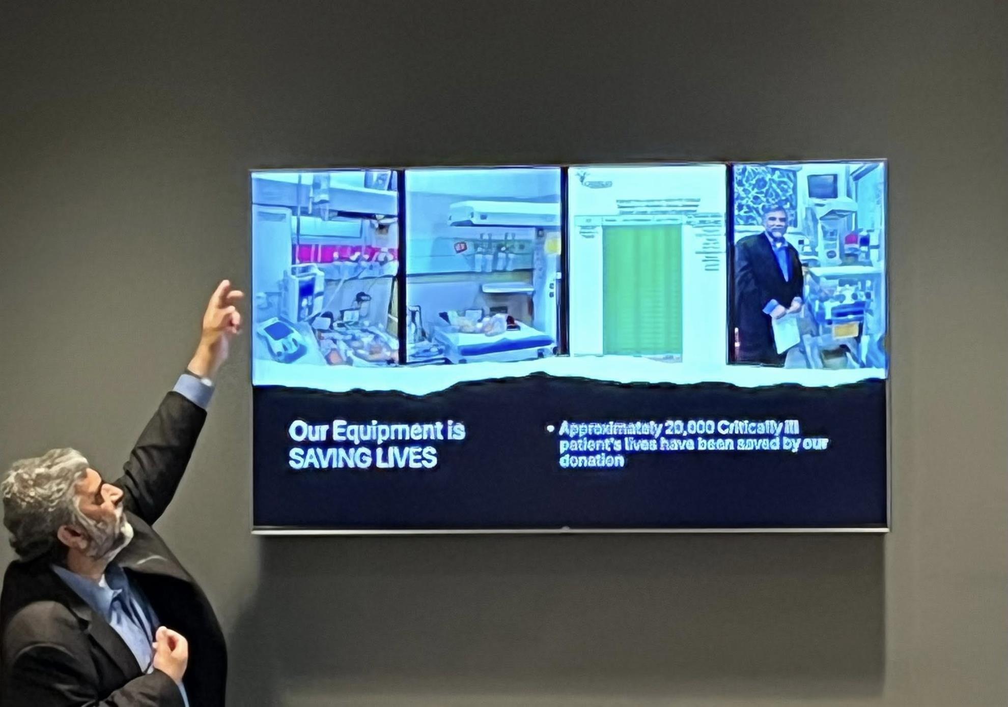 Masroor Malik, dressed in a black suit with a light blue button-down shirt, describing a slide in his presentation. The slide is titled, 