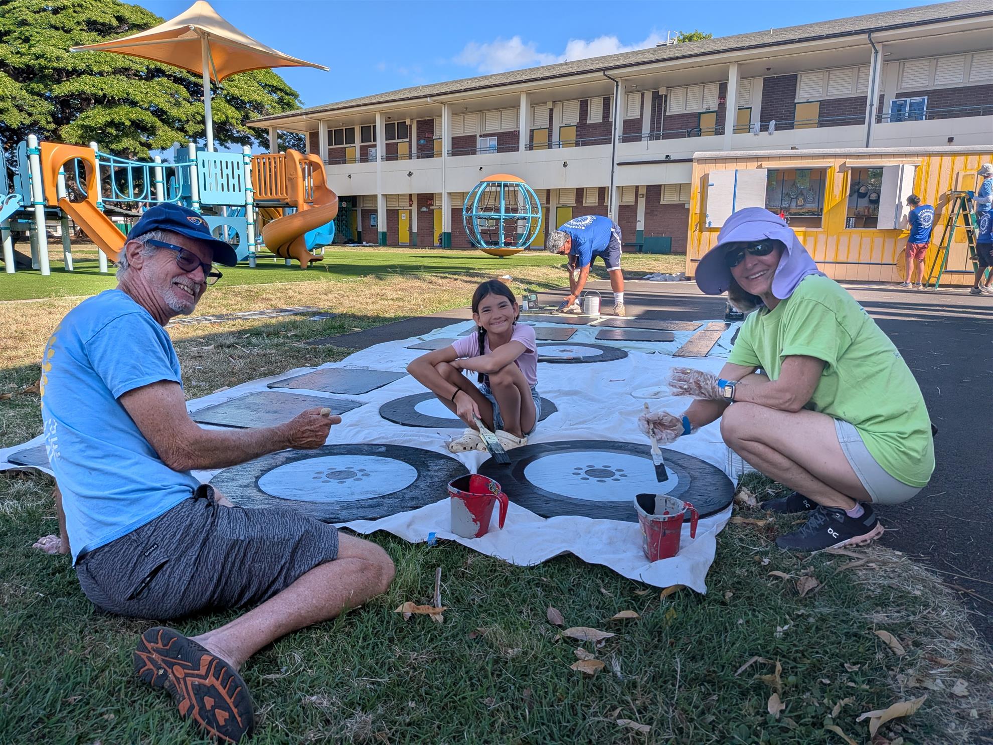 Volunteers painting the bus wheel panels on a ground covering