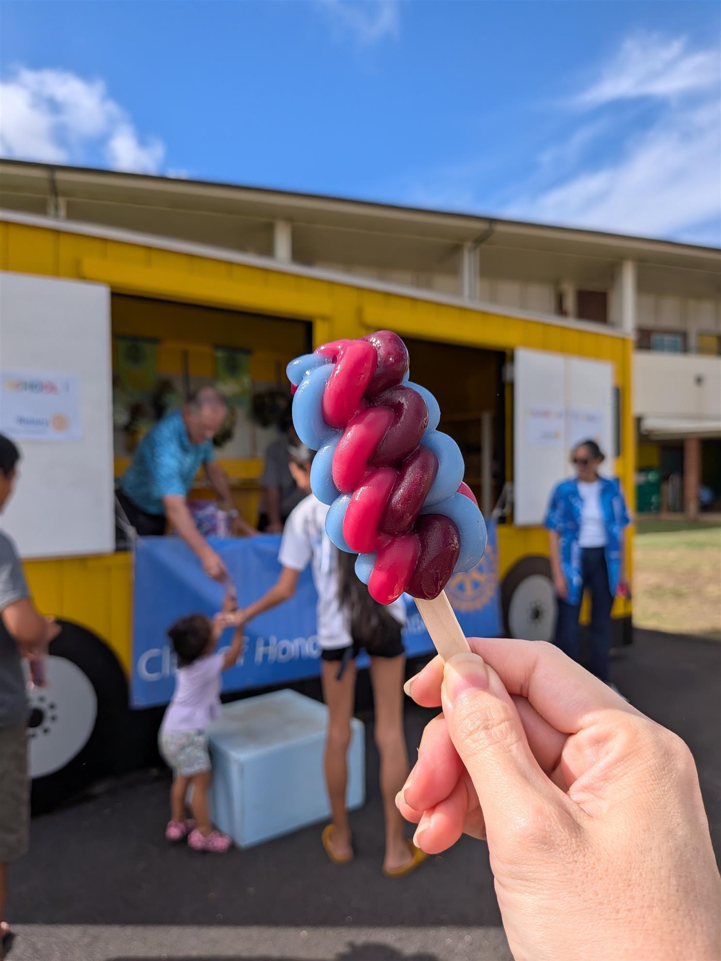 A colorful frozen treat held in front of the Peacock Bus