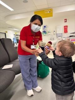 A FONE volunteer hands a small toy to a young patient in the Emergency Department