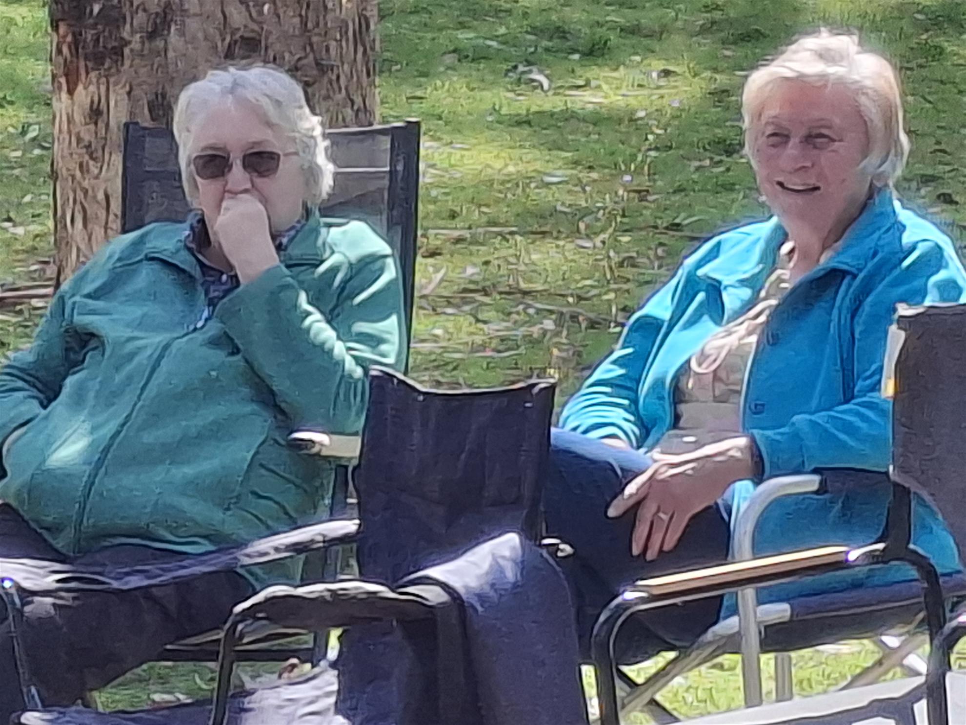 Two attendees relaxing in camp chairs, chatting and laughing