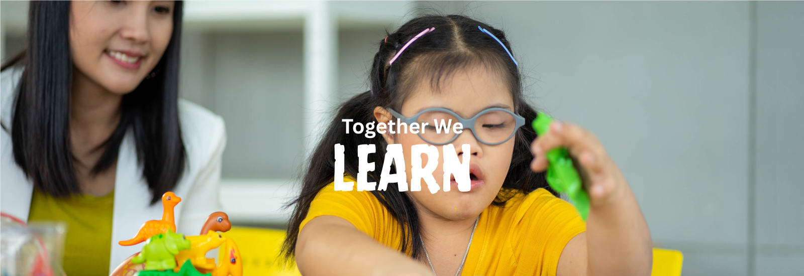 Young girl with Down syndrome plays with toy animals as an adult smiles. “Together, We Learn.”
