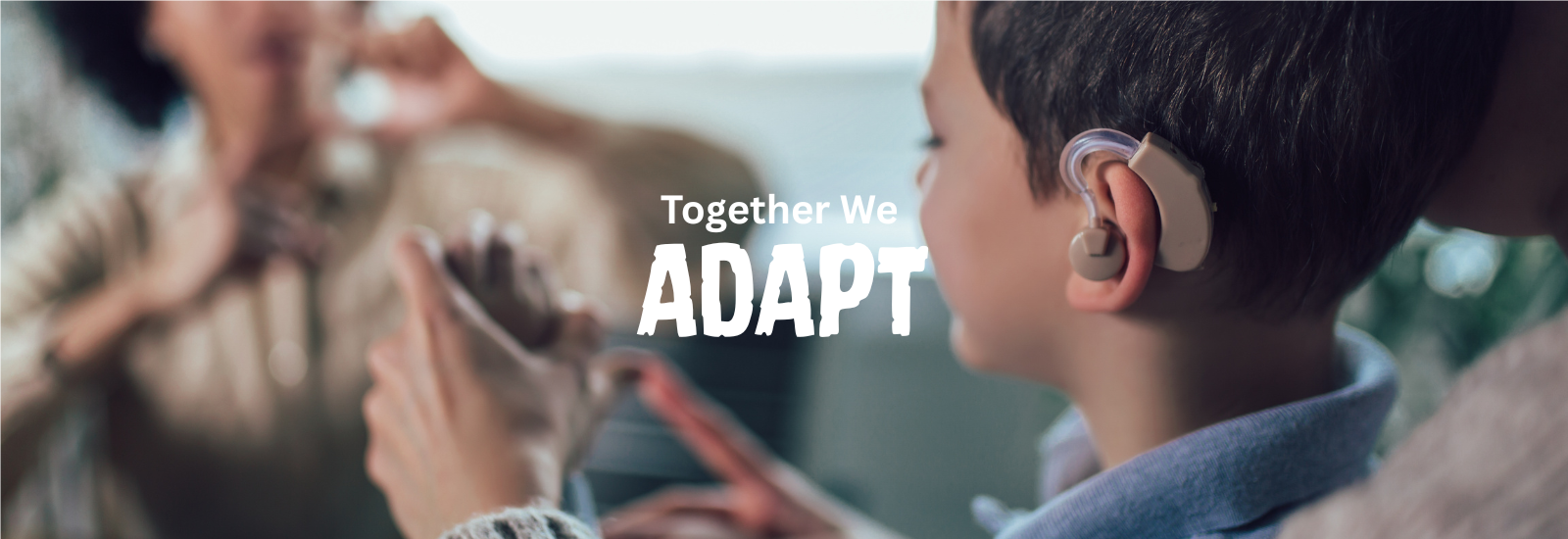 Child with a hearing aid watches an adult signing. “Together, We Adapt.”