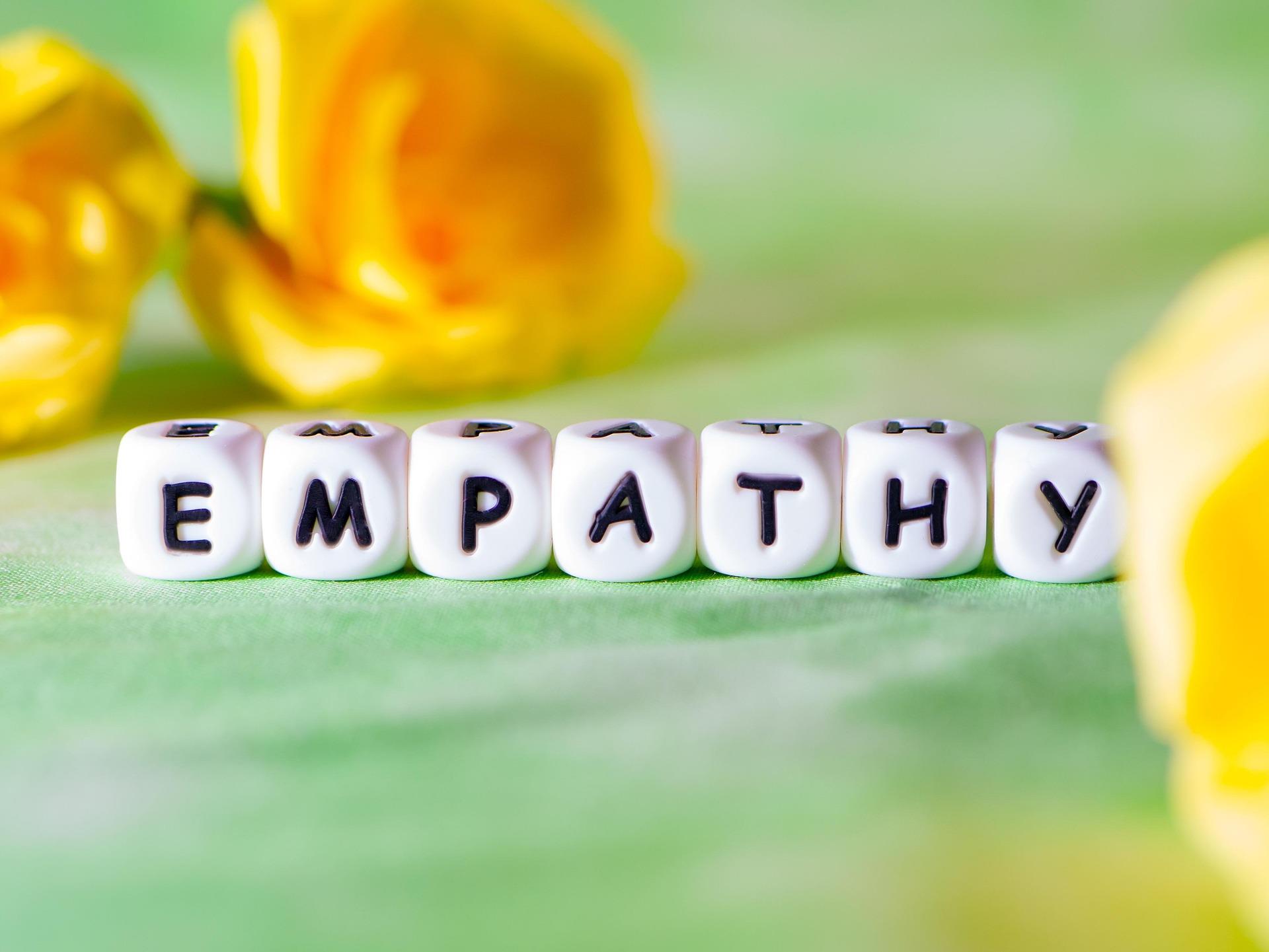 White letter cubes spelling the word empathy on a soft green background with blurred yellow flowers in the distance.
