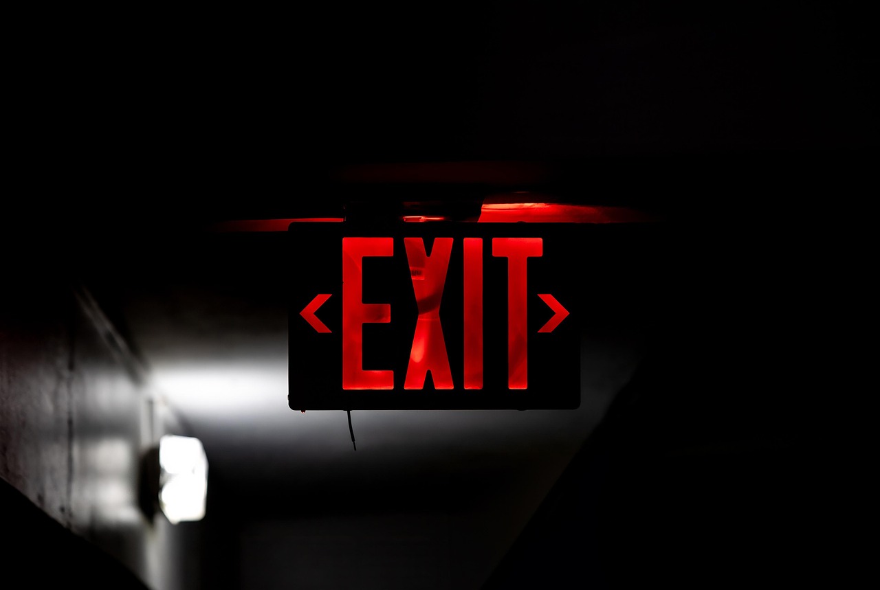 A red illuminated exit sign suspended in a dark corridor, symbolizing emergency response and evacuation.