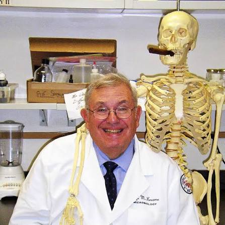 Professor Michael Kossove smiling in a white laboratory coat beside a human skeleton model