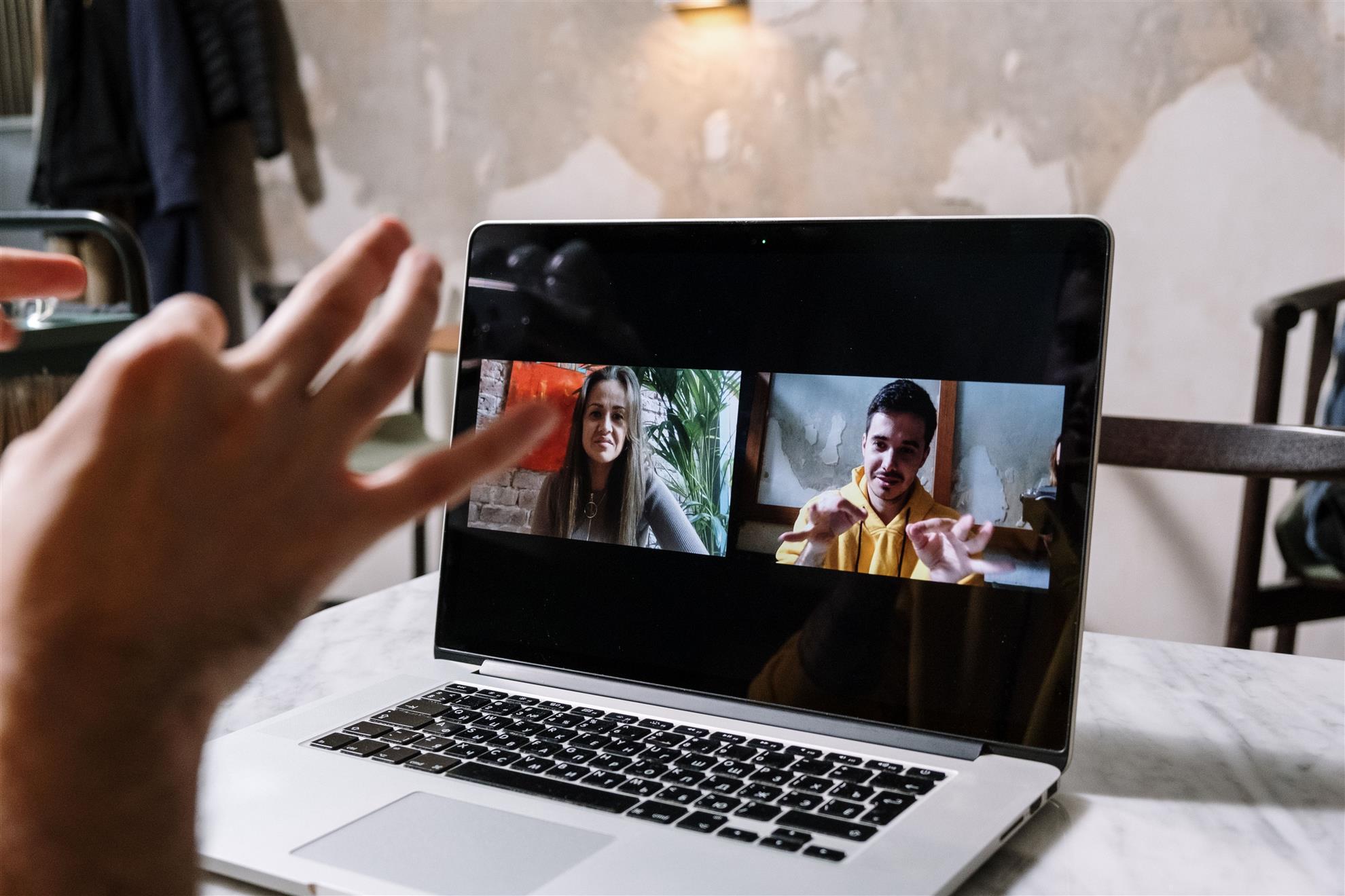 A person waving during a video call with two participants on a laptop.