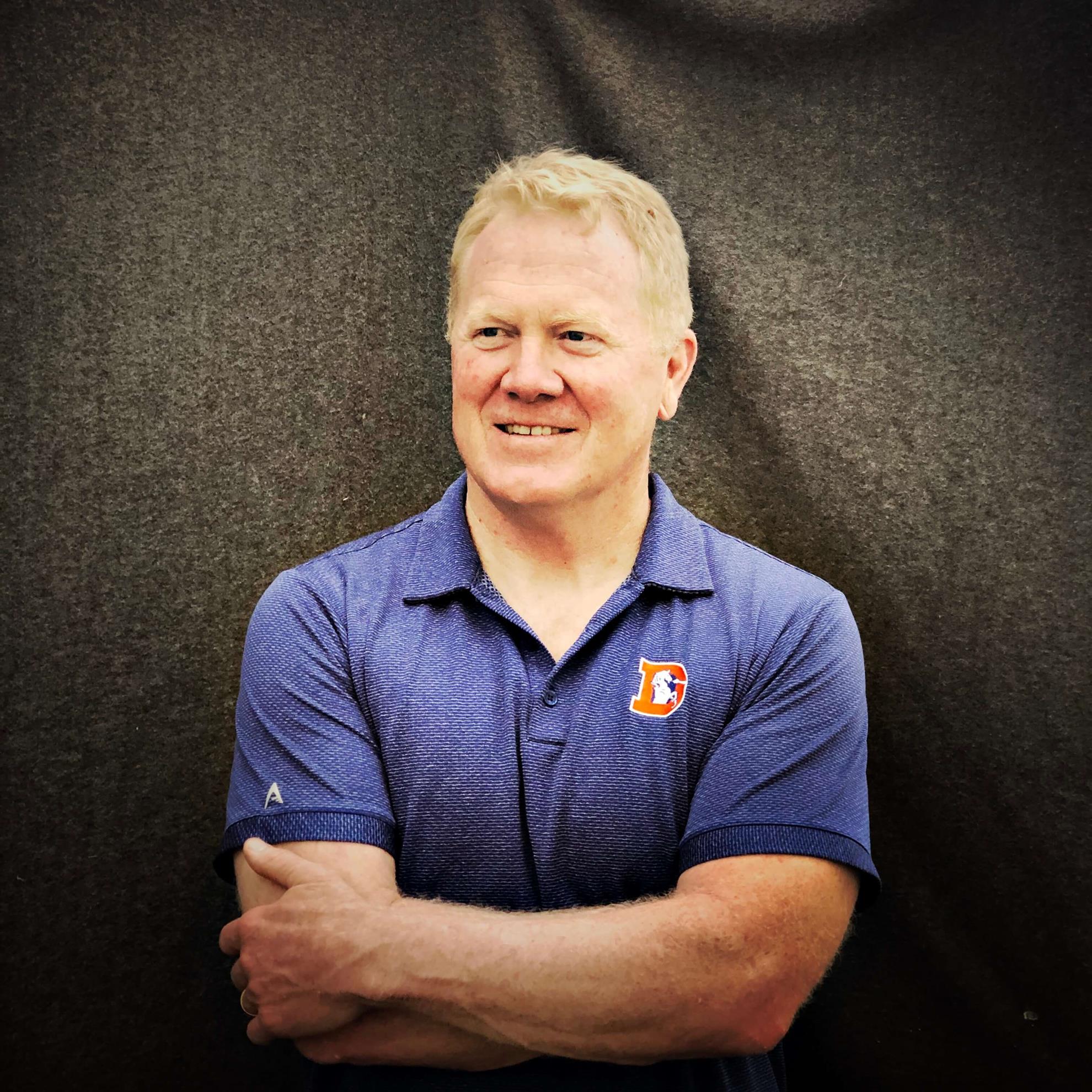 photo of Karl Mecklenburg in a blue Denver Broncos shirt standing in front of a gray background