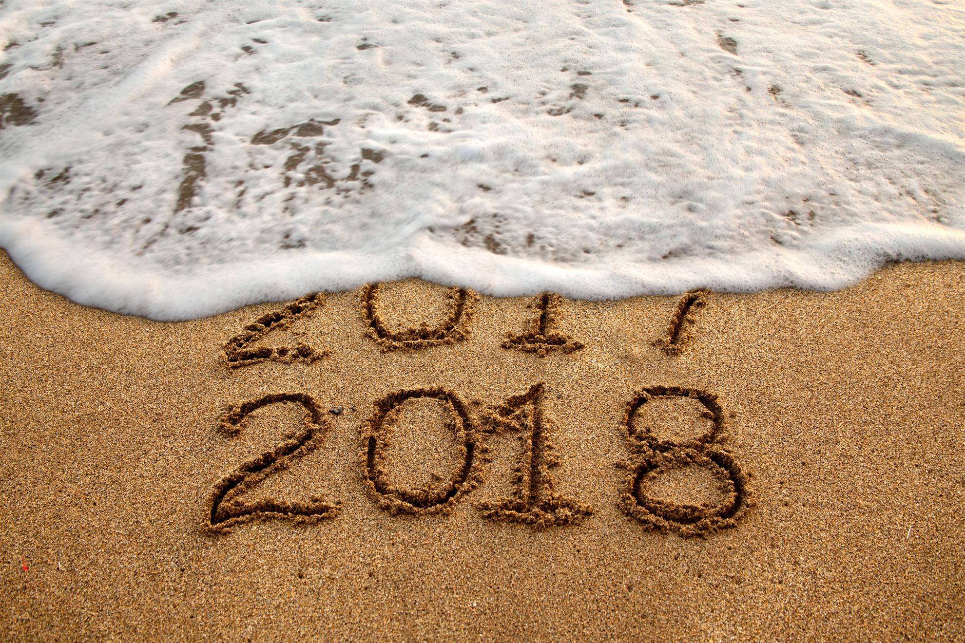 Water washes across the beach, where 2017 2018 are written in sand.
