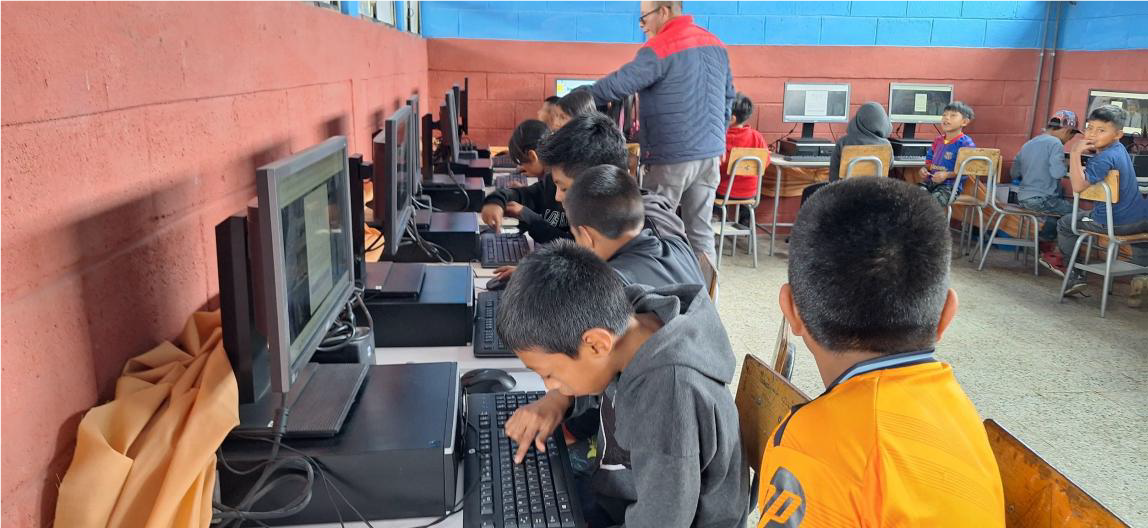 Students at a computer lab in a Guatemalan school, with a teacher helping in the background