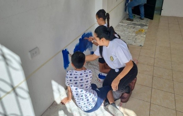 A Rotary club member working alongside a young student to paint a school wall