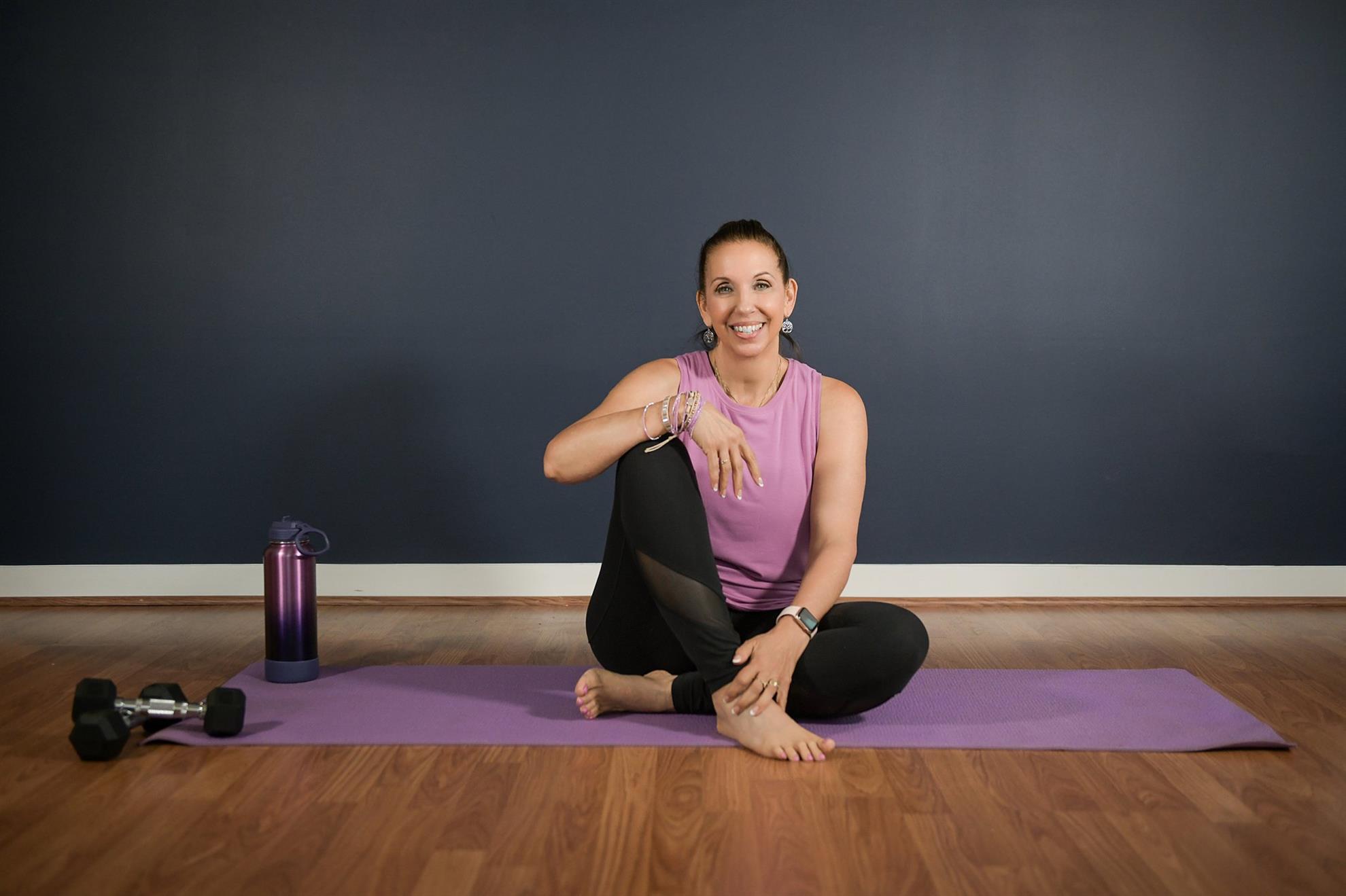 A smiling woman on a yoga mat looks at the camera.