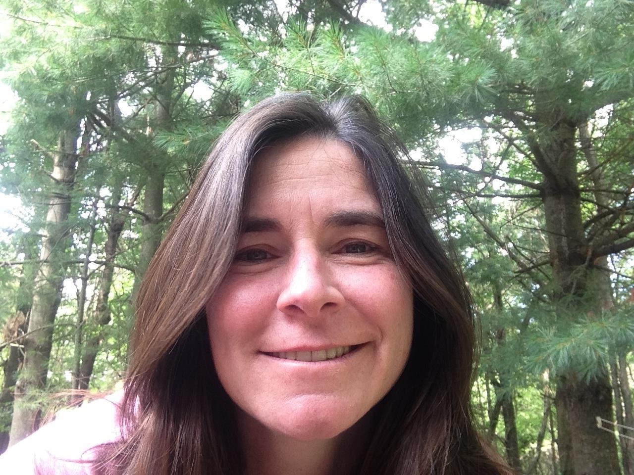 Headshot of Audra Kaplan, a white woman with straight brown hair smiling in the woods